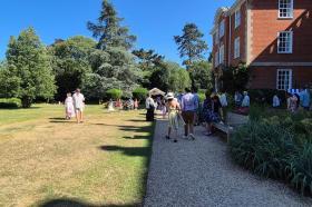 Guests strolling through the LMH gardens in bright summer sunshine during the 2025 Alumni Garden Party, with families and alumni gathered near the red-brick building.