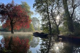 Boats on the River Cherwell at Lady Margaret Hall, Oxford, with morning mist rising and autumn trees reflected in the water.