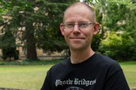 Peter Thonemann, who has very short brown hair, rimless glasses and is wearing a black t-shirt with 'Phoebe Bridgers' printed on it