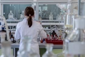 A photo of a woman wearing a white lab coat standing in a lab full of test tubes and other scientific equipment