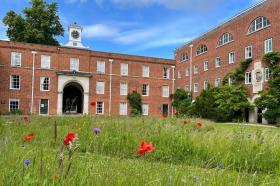 Lady Margaret Hall’s Wolfson Quad with red brick buildings, clock tower, and wildflowers in the foreground