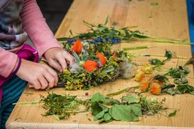 A table covered in autumn-coloured cut flowers, and someone mostly out of shot making an arrangement out of them