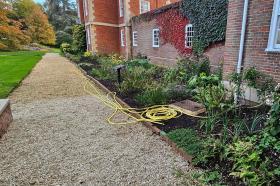 A gravel path alongside a half-planted garden border, with a yellow hosepipe in the foreground