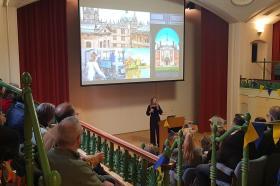 A lecture theatre decorated with blue and yellow bunting, with the audience watching a presentation about life at Oxford