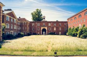 A view of LMH's Talbot Quad, looking across a wildflower meadow towards red brick buildings with a clock tower