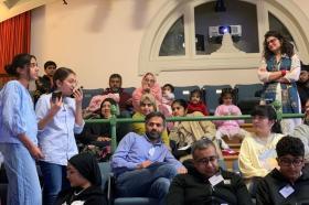 A group of mainly British-Pakistani and British-Bangladeshi families standing inside a lecture theatre at Lady Margaret Hall
