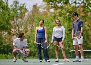 A group of four students standing on a blue hard-court tennis court in the LMH gardens