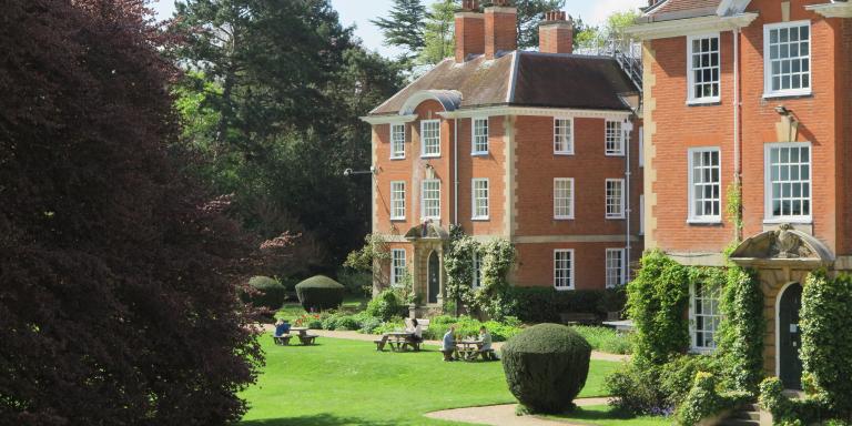 Student studying outside on picnic benches with red brick buildings in the background