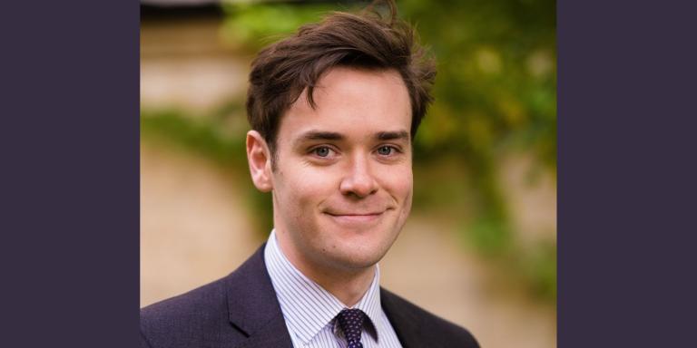 Joshua Bennet, who has short dark brown hair, wearing a dark suit and tie