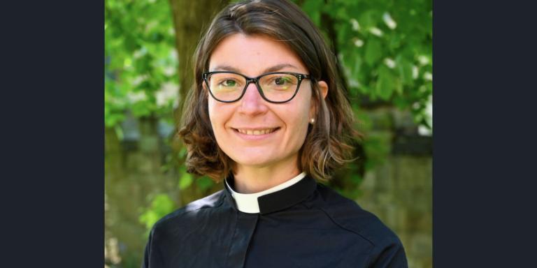 Stephanie Burette, who has shoulder-length brown hair, glasses and is wearing clerical dress