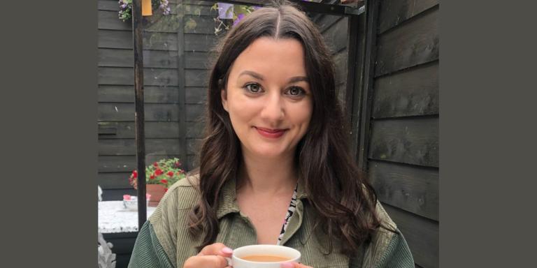 A woman with long dark brown hair sitting in a garden with a cup of tea