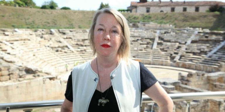 A.E. Stallings, a woman with short blonde hair, stands in front of a greek ampitheatre