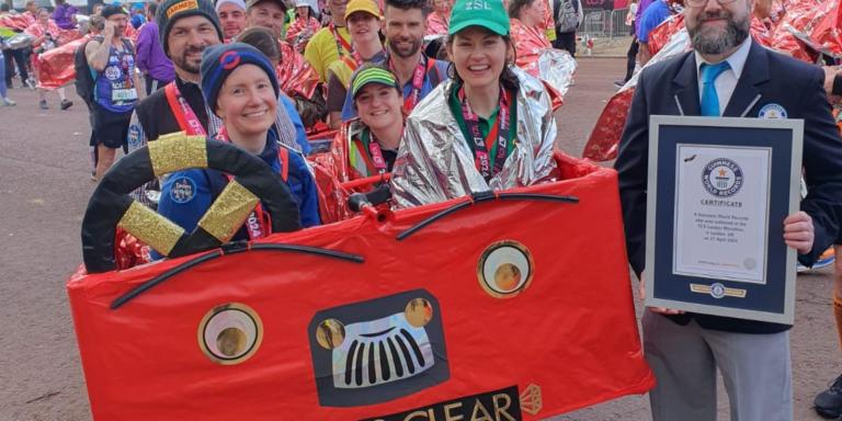A photo of runners at the London marathon in a 10-person red bus costume being awarded a Guinness World Record certificate