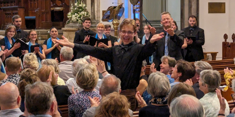 A young man with short light brown and glasses has just conducted a rendition of an original musical composition 