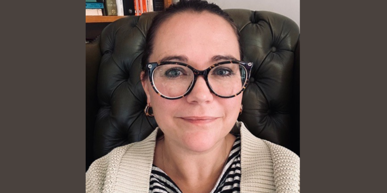 Dr Sophie Nicholls, who has dark brown hair tied back in a ponytail and dark-framed glasses, sitting in her office