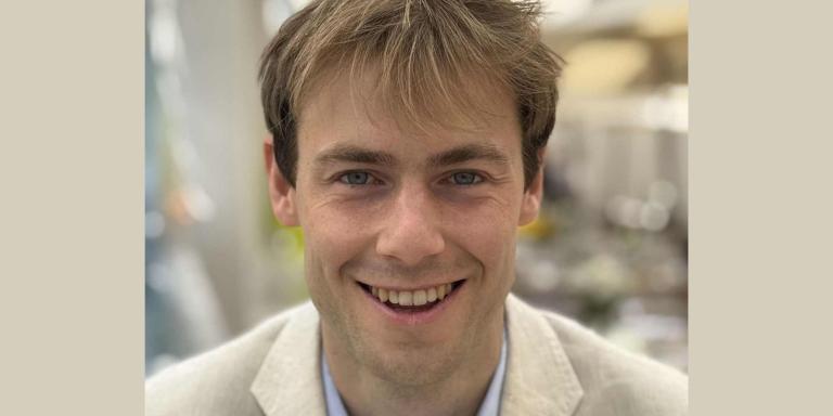 Thibault Rushbrookm who has short sandy brown hair and is wearing a pale coloured suit, smiles at the camera