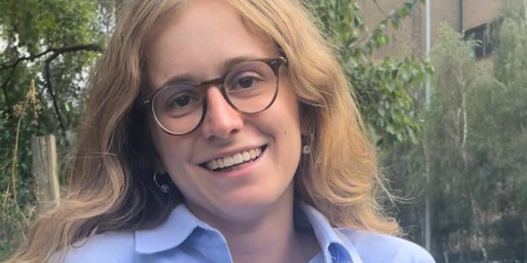 Ariadne Pagoni, who has long light brown hair and is wearing dark framed glasses, smiles at the camera