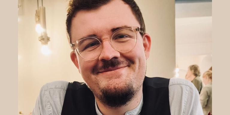 Florian Lutzelberger, who has short dark hair and a dark beard and moustache and clear-framed glasses is smiling at the camera