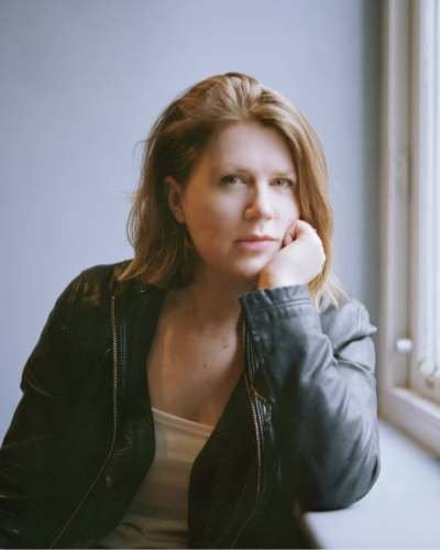 Photographic portrait of Professor Sophie Ratcliffe, who has shoulder-length blonde hair and is wearing a dark leather jacket
