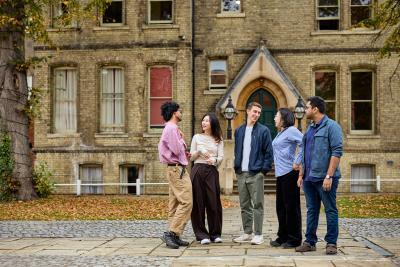 A group of students stand as a group looking at each other warmly in an open square.