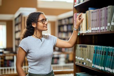A student reaches to a shelf in the library and takes a book.