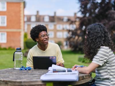Two students sitting at a wooden table in the LMH gardens with books and laptops in front of them