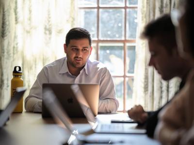 A tutor behind a laptop explains to students seated around a table.
