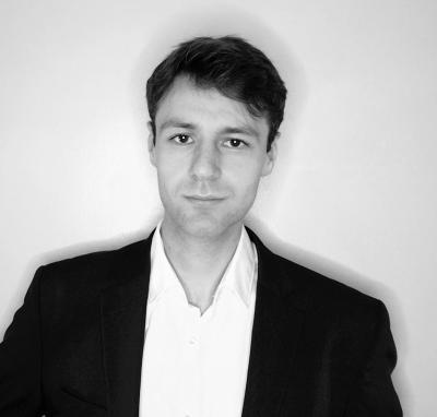 Black and white headshot of Athanasios Peftinas, who has short dark hair and is wearing a white shirt and black suit jacket