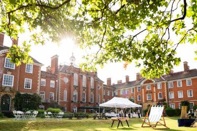 A photo of Lady Margaret Hall, with the sun setting behind the building and a party tent set up on the lawn.