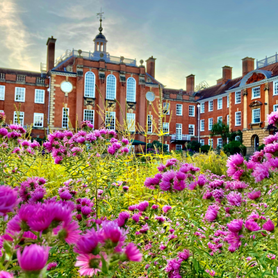 A grand Edwardian building with intricate windows overlooks a garden with purple flowers in the foreground.
