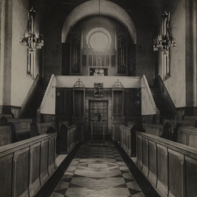 A black and white photo of the interior of a Chapel, with high ceilings and a large round window on the far wall