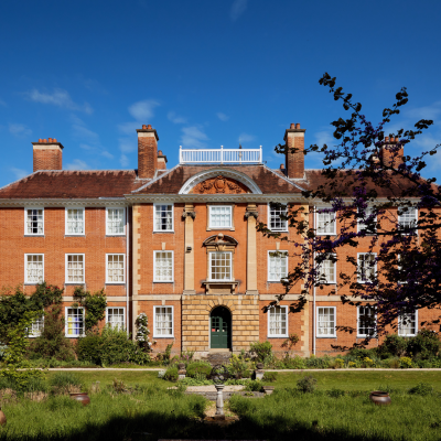A red-brick Edwardian building with symmetrical architecture overlooks a sunken garden with an armillary sphere in the centre