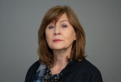Portrait of Professor Christine Gerrard, wearing a dark sweater and patterned scarf, against a plain grey background