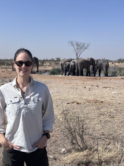 A mid shot of Jessica with elephants grazing in the background